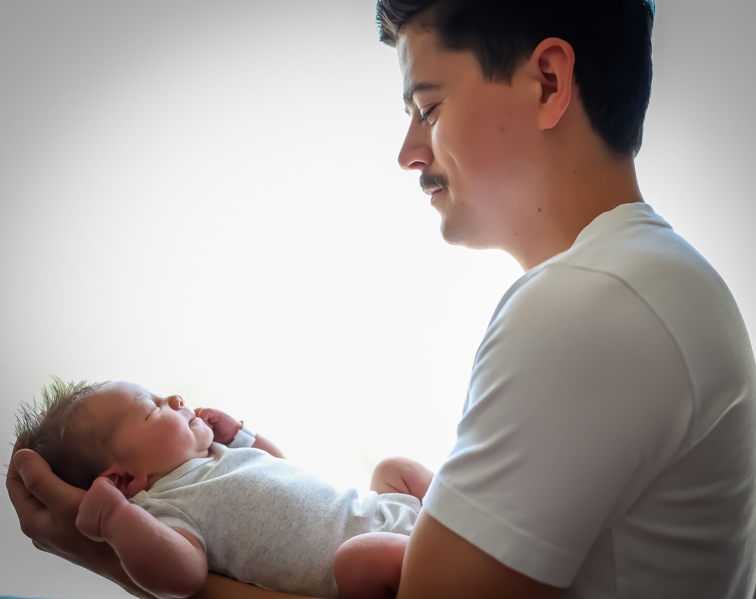 Series showing tender interaction with newborn baby in white setting.