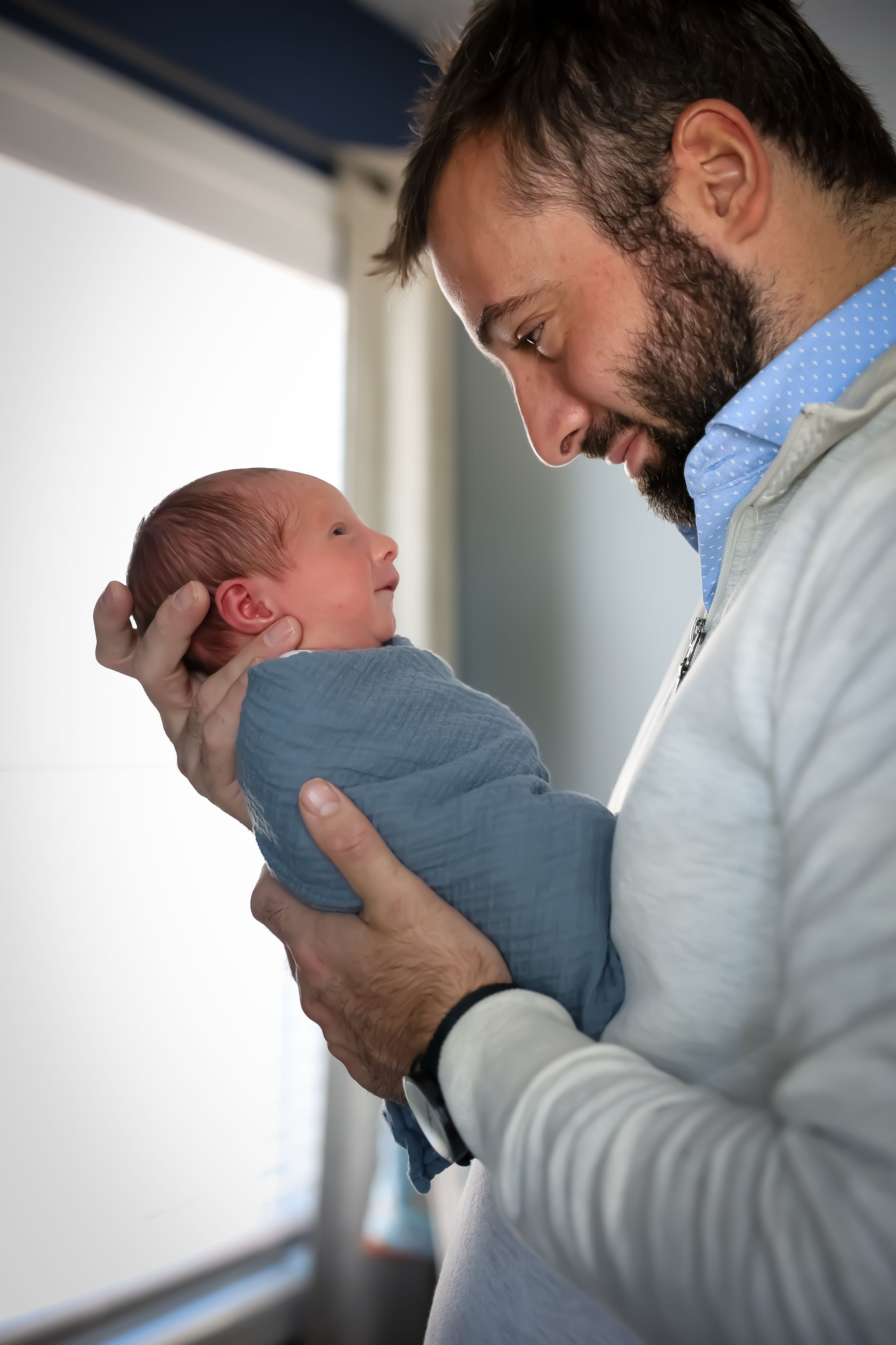 Tender moments captured between parent and newborn in natural window light.