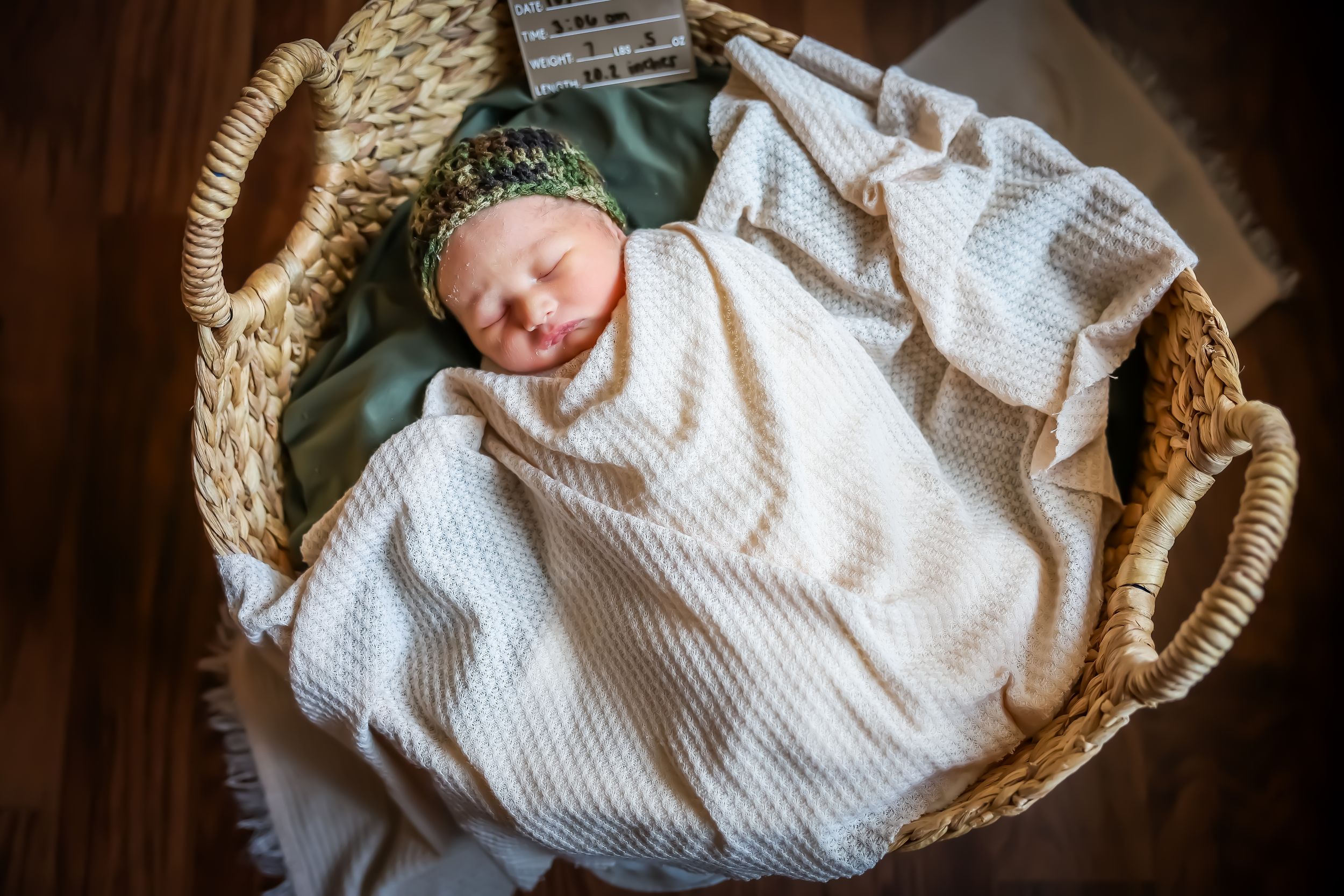 Peaceful newborn sleeping in rustic woven basket with white textured blanket.