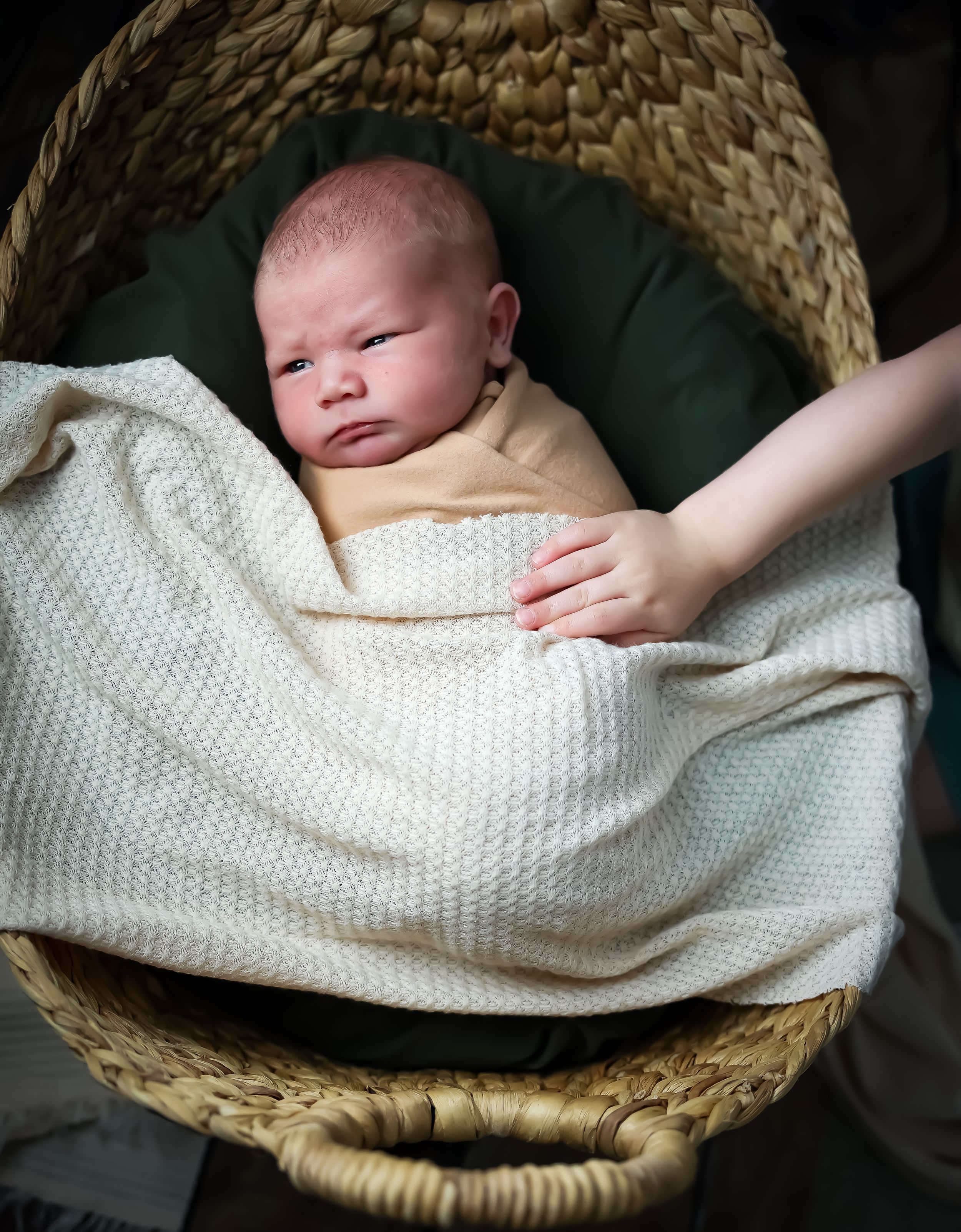 A newborn baby resting peacefully in a woven basket with a white knit blanket.