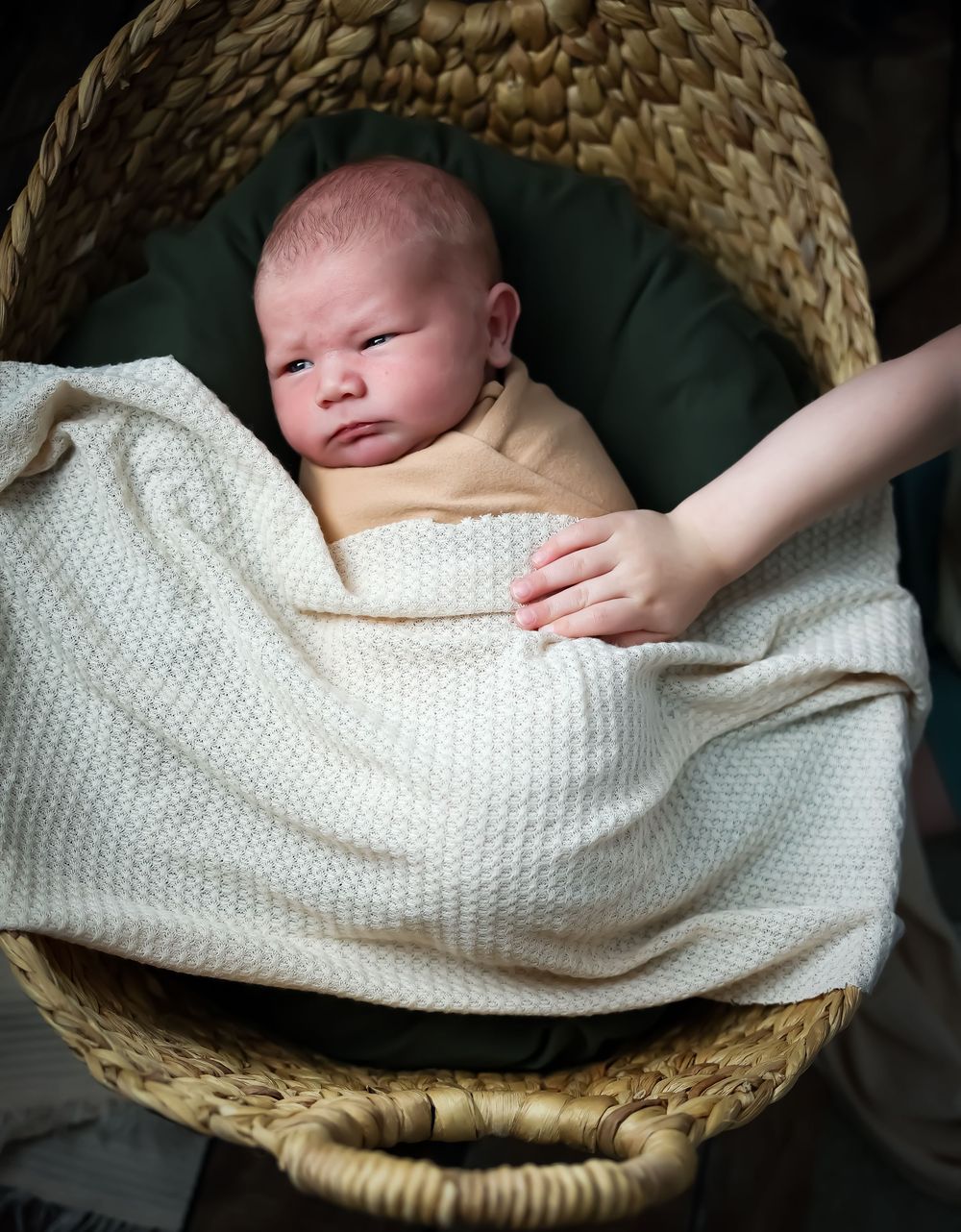 A newborn baby resting peacefully in a woven basket with a white knit blanket.