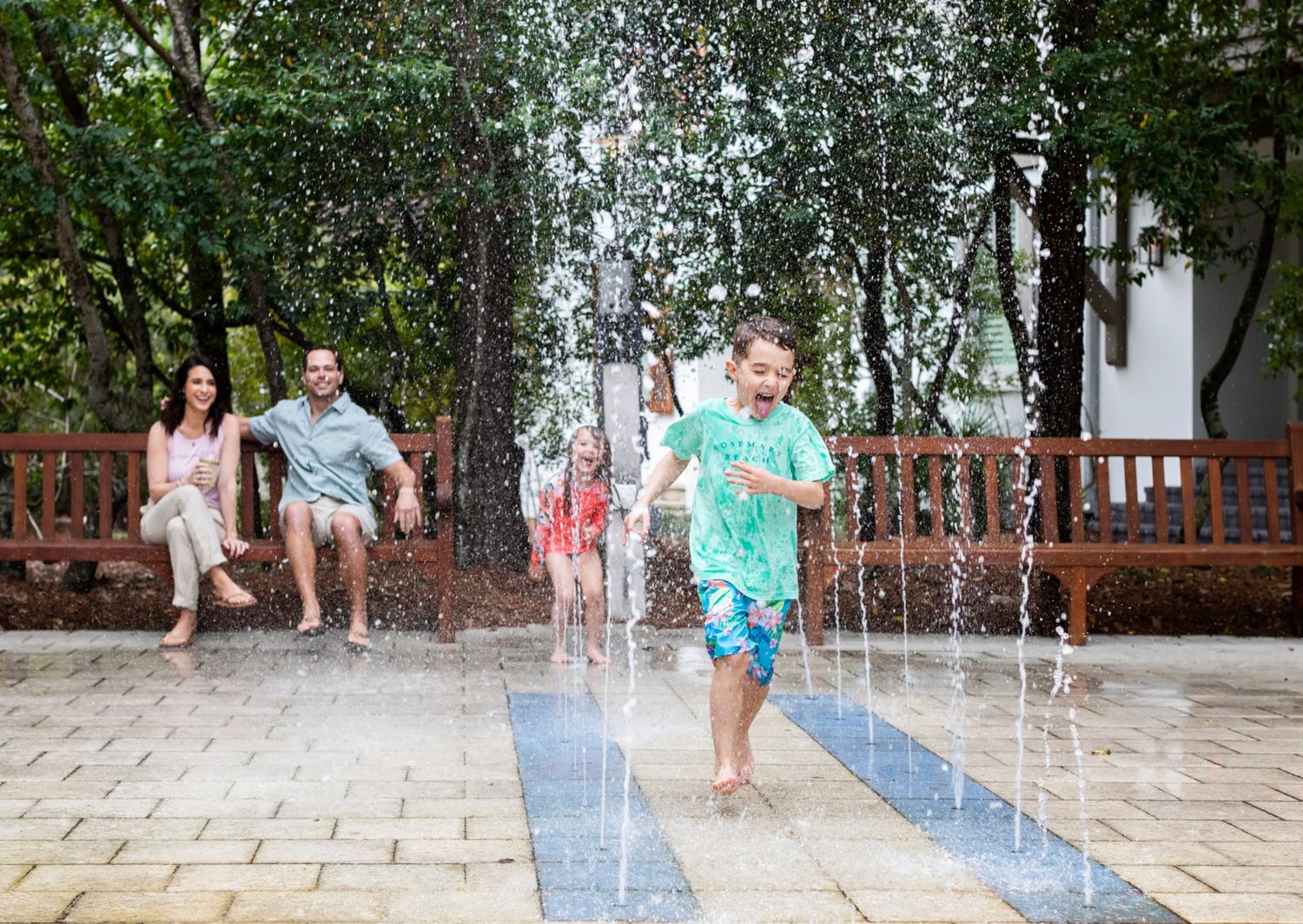 Children play and splash in outdoor water fountains on a hot summer day at a public plaza.