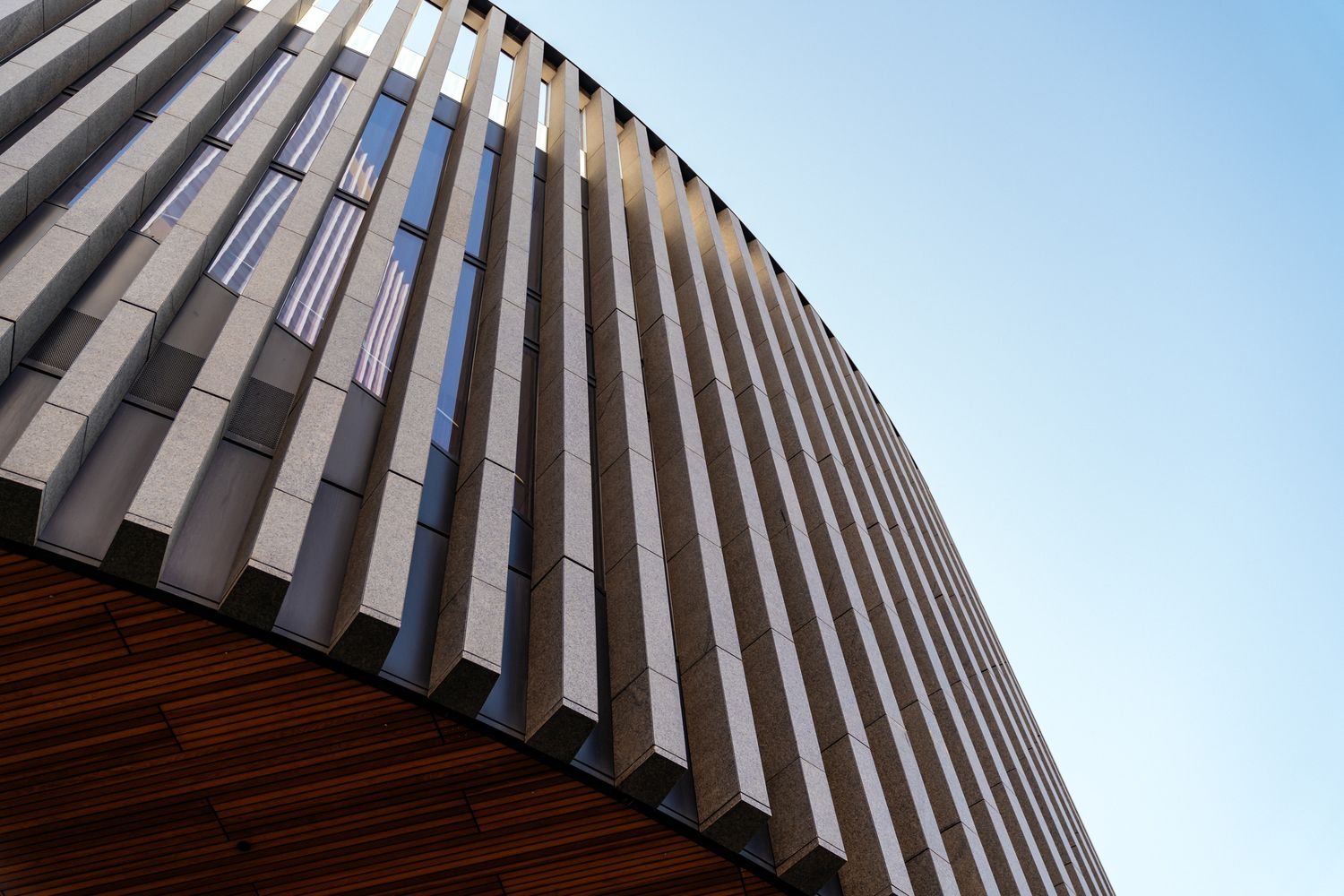 Modern architectural detail showing curved wooden slats against a blue sky.