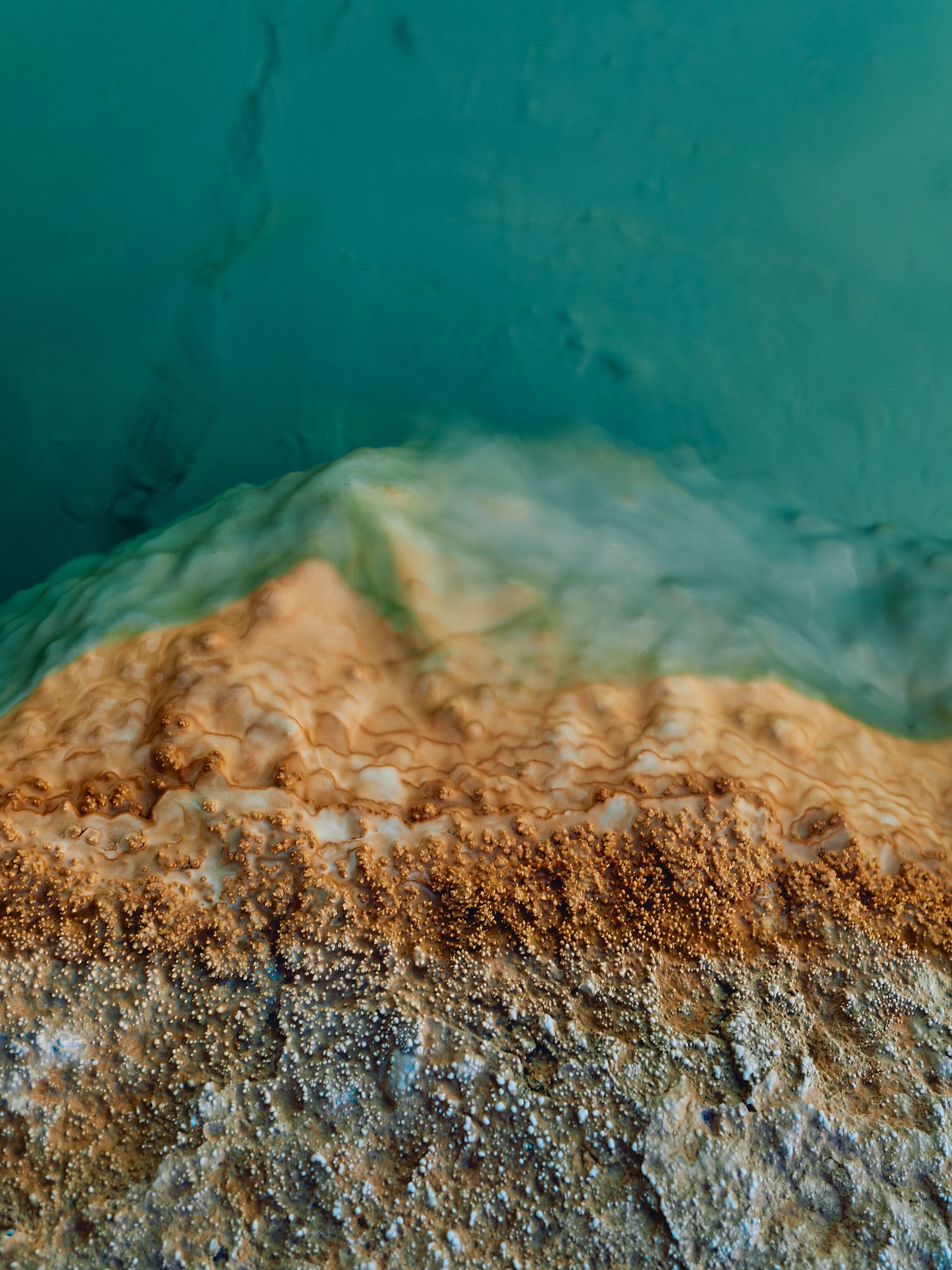 Close-up macro photograph of mineral deposits with turquoise water showing natural textures and sediment layers.