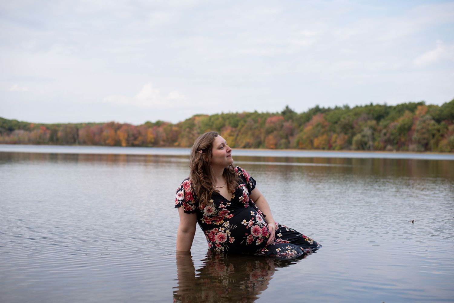 A beautiful moody photo of a pregnant woman sitting in the water of a lake in autumn/fall by Aslyn O Photo.