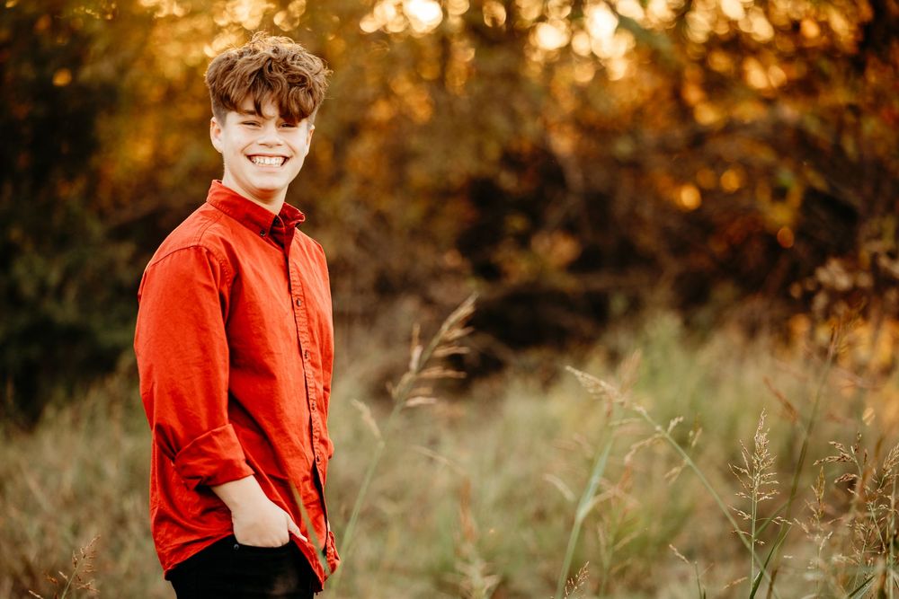A child in a bright red shirt stands in a golden autumn field during sunset.