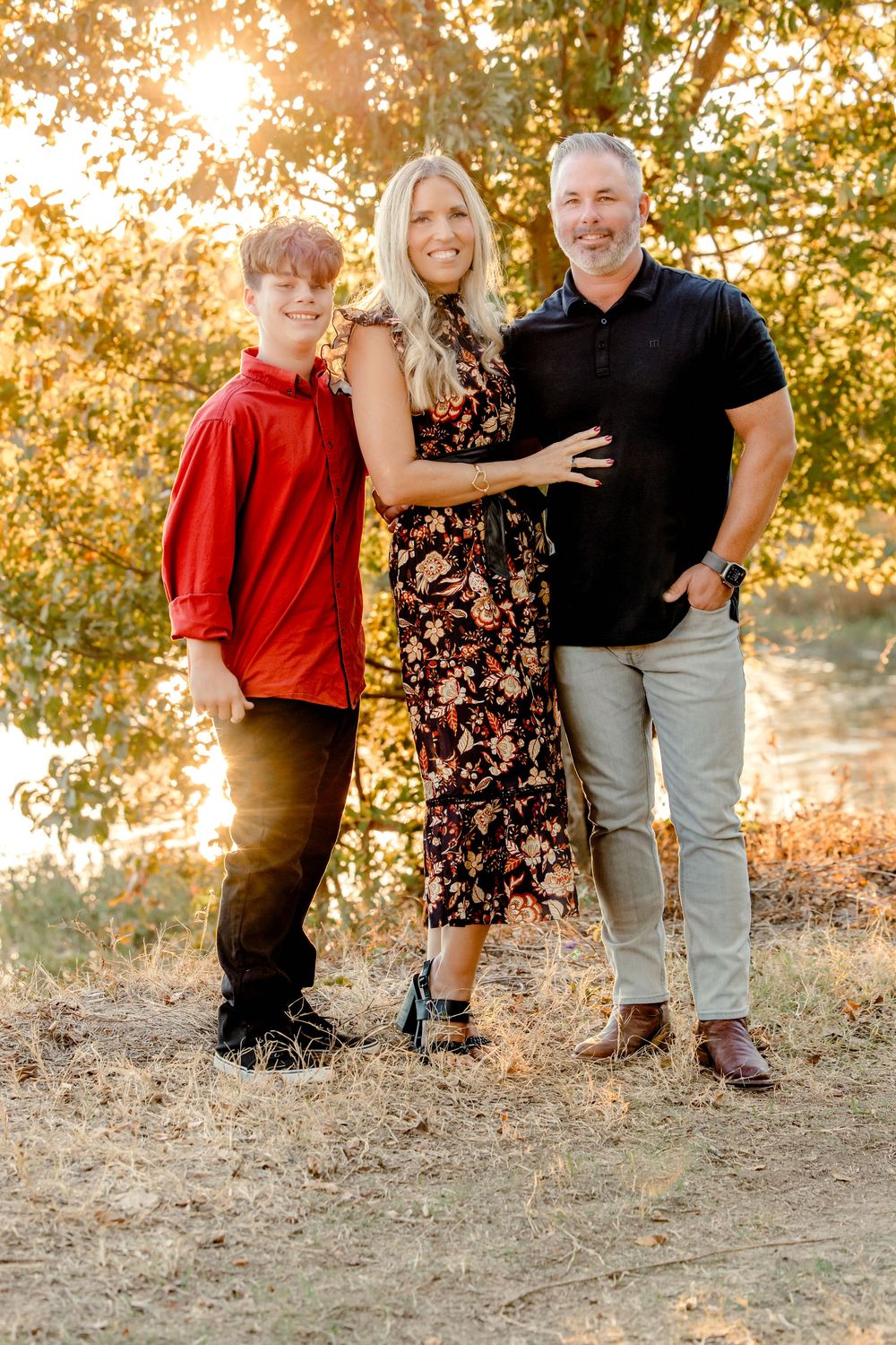 Three people pose together in a warm sunset glow on a grassy hillside wearing casual clothing.