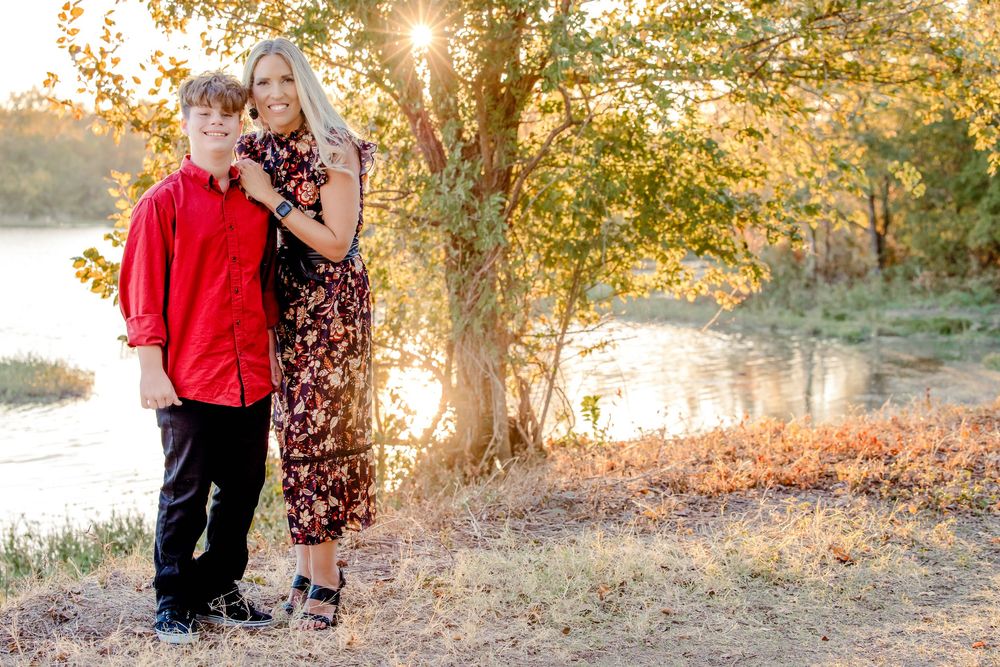 A couple shares a tender moment at sunset by a lake with golden sunlight filtering through autumn trees.