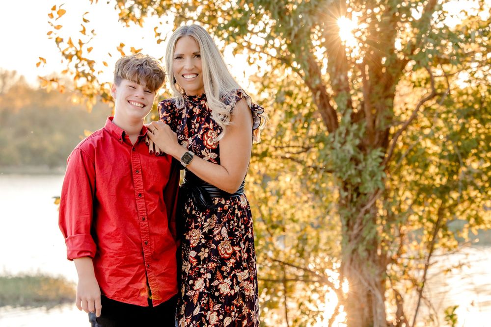 Couple in coordinating red and black outfits pose together in golden sunlit outdoor setting during autumn.