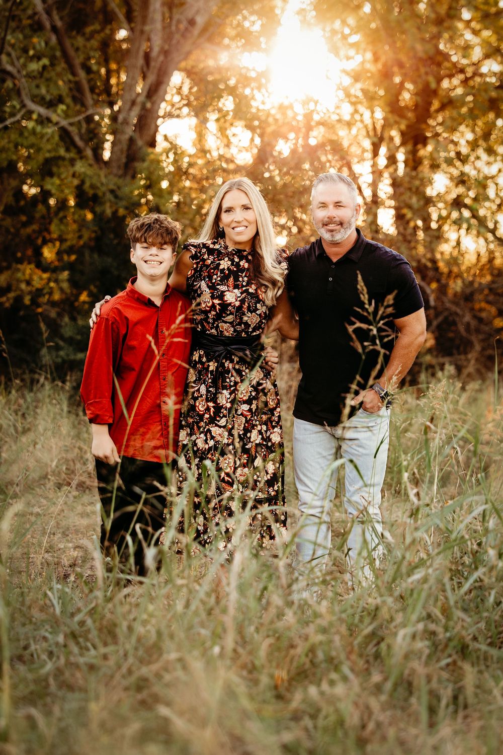 A family poses together in a golden-lit field during sunset while wearing coordinated red and floral outfits.