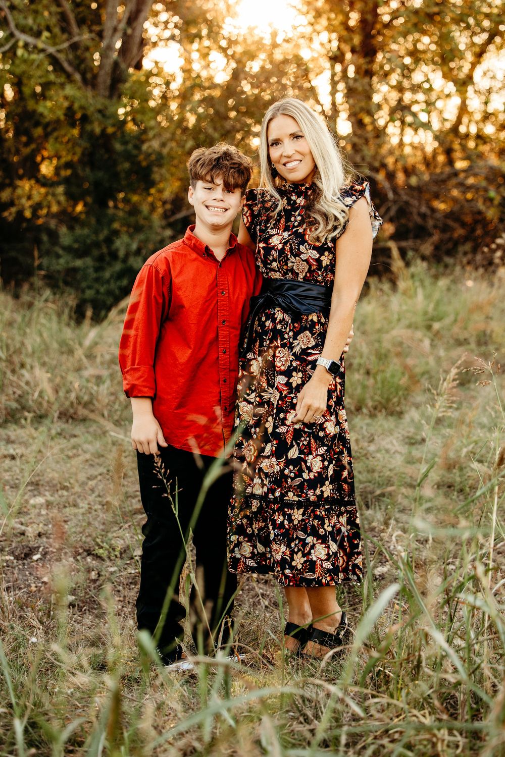 Two people pose together in a field at sunset wearing red and floral outfits.