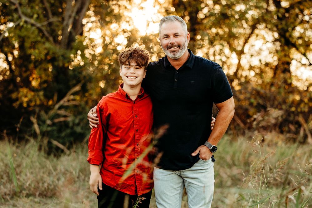 A person in a red shirt and someone in a black polo stand together outdoors during golden hour sunset.