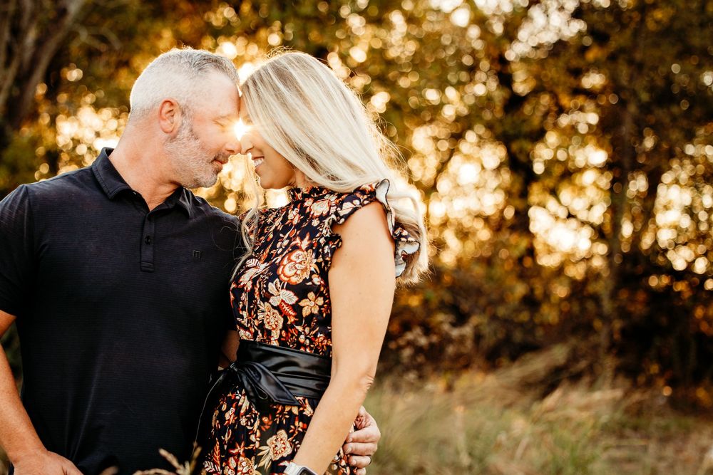 A couple shares an intimate moment in a golden sunset field wearing black and lace outfits.