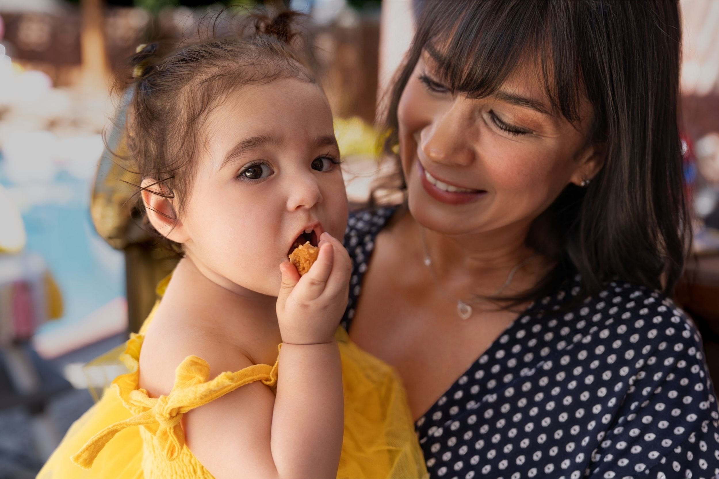 A parent and child share a tender moment together as the child eats while wearing a yellow dress.
