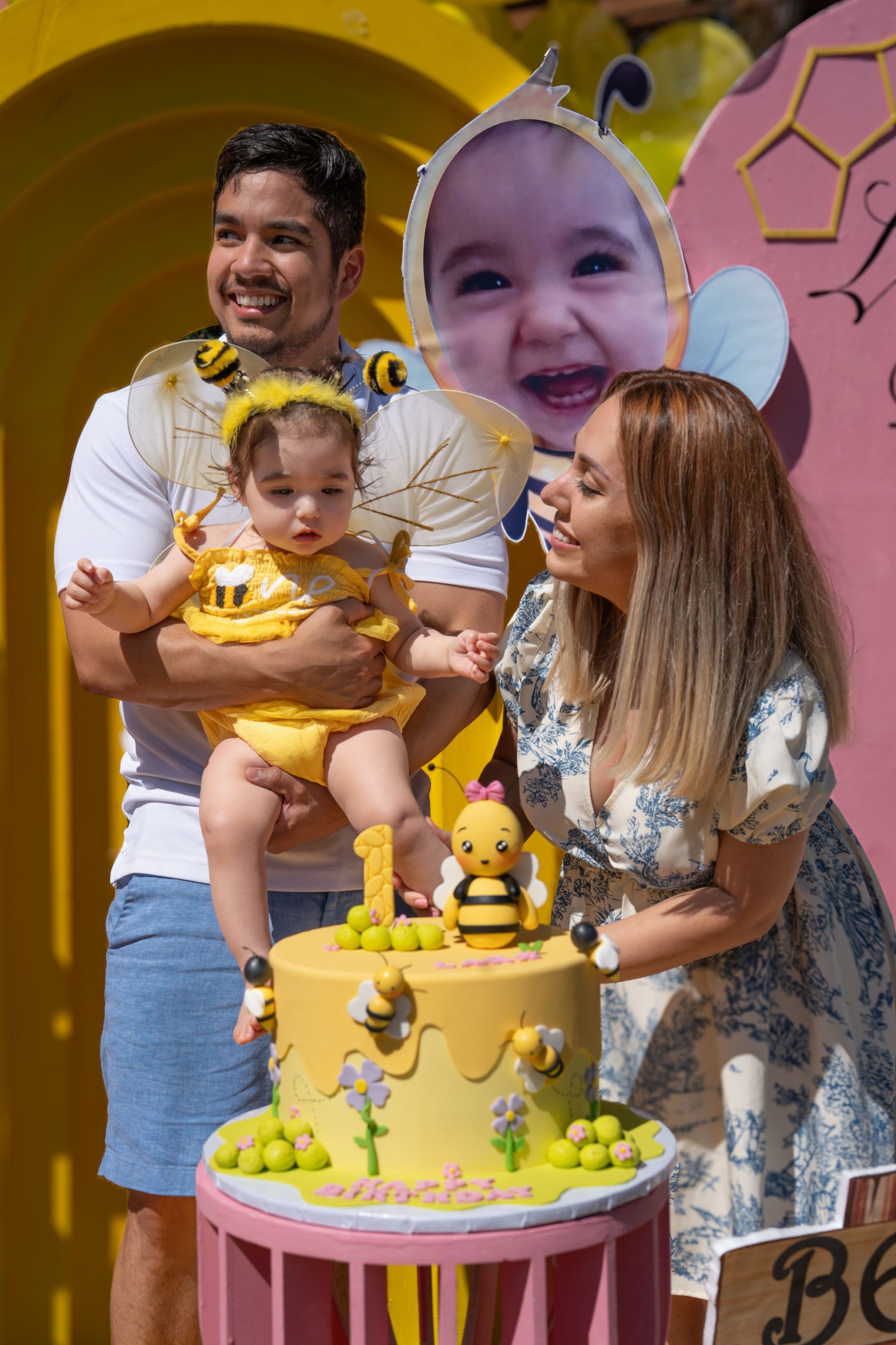 Baby in yellow bee costume celebrates first birthday with yellow themed cake and decorations.