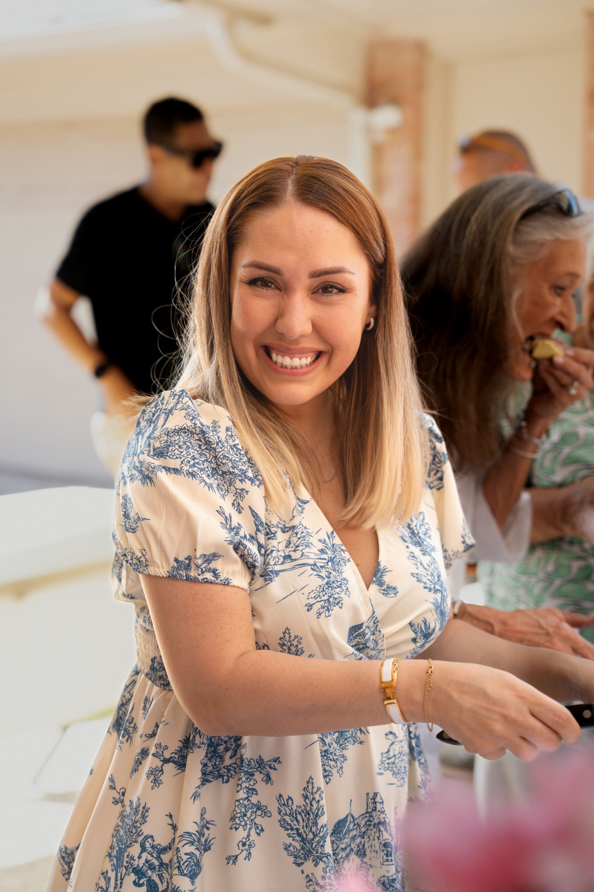 A person in a floral dress reaching forward at what appears to be a social gathering.