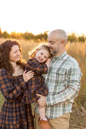 A family shares a tender moment together in a sunlit field during golden hour. Nj Family Photographer in Sussex County