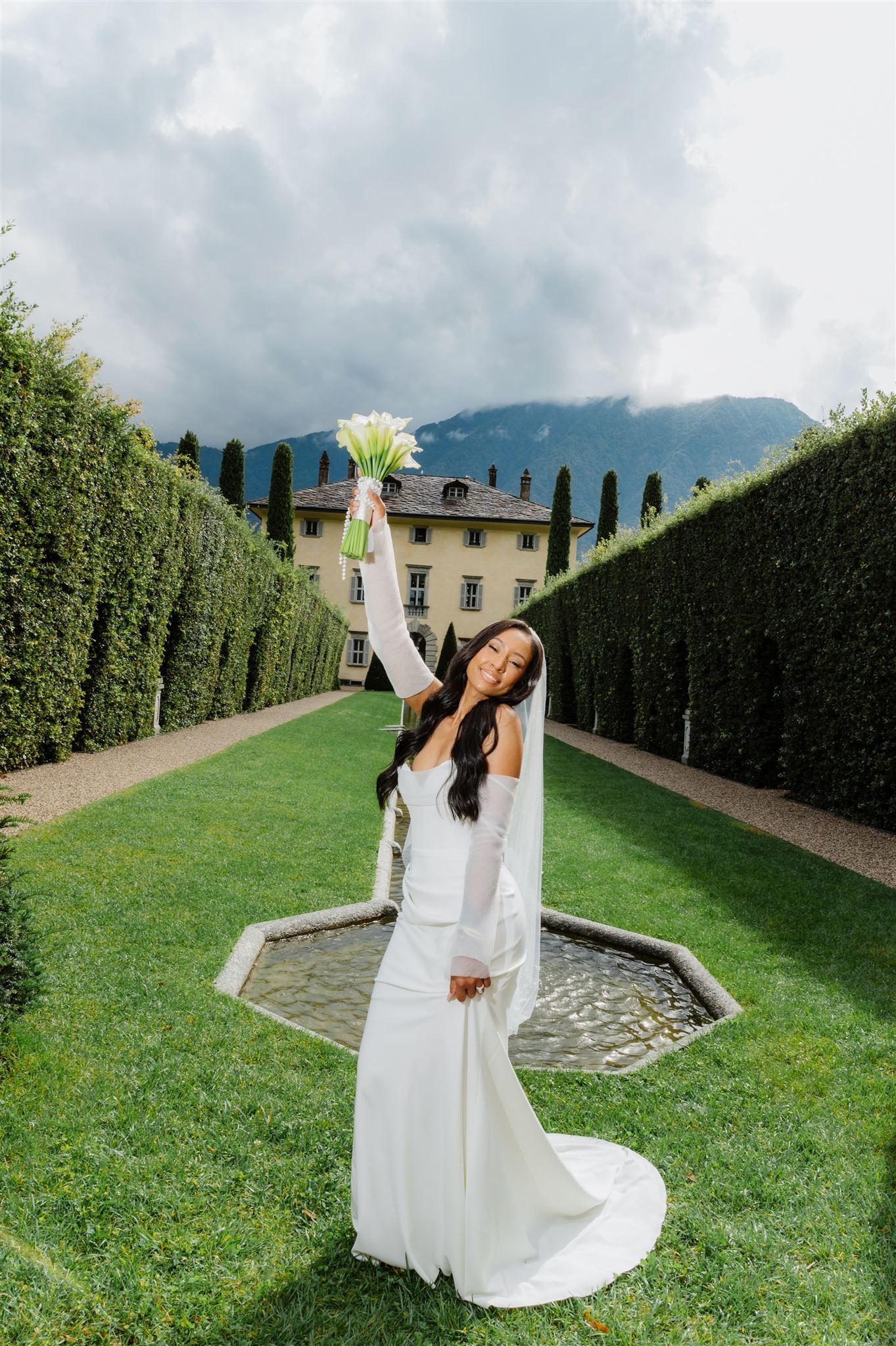 Wedding celebration in elegant garden with tall hedges and mountain views.