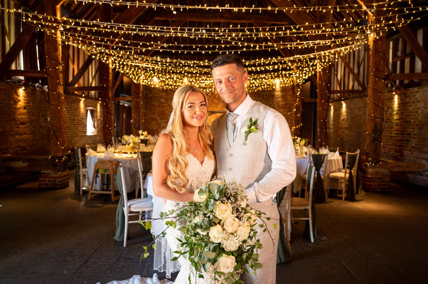 Rustic barn wedding reception venue decorated with romantic string lights and white floral arrangements.