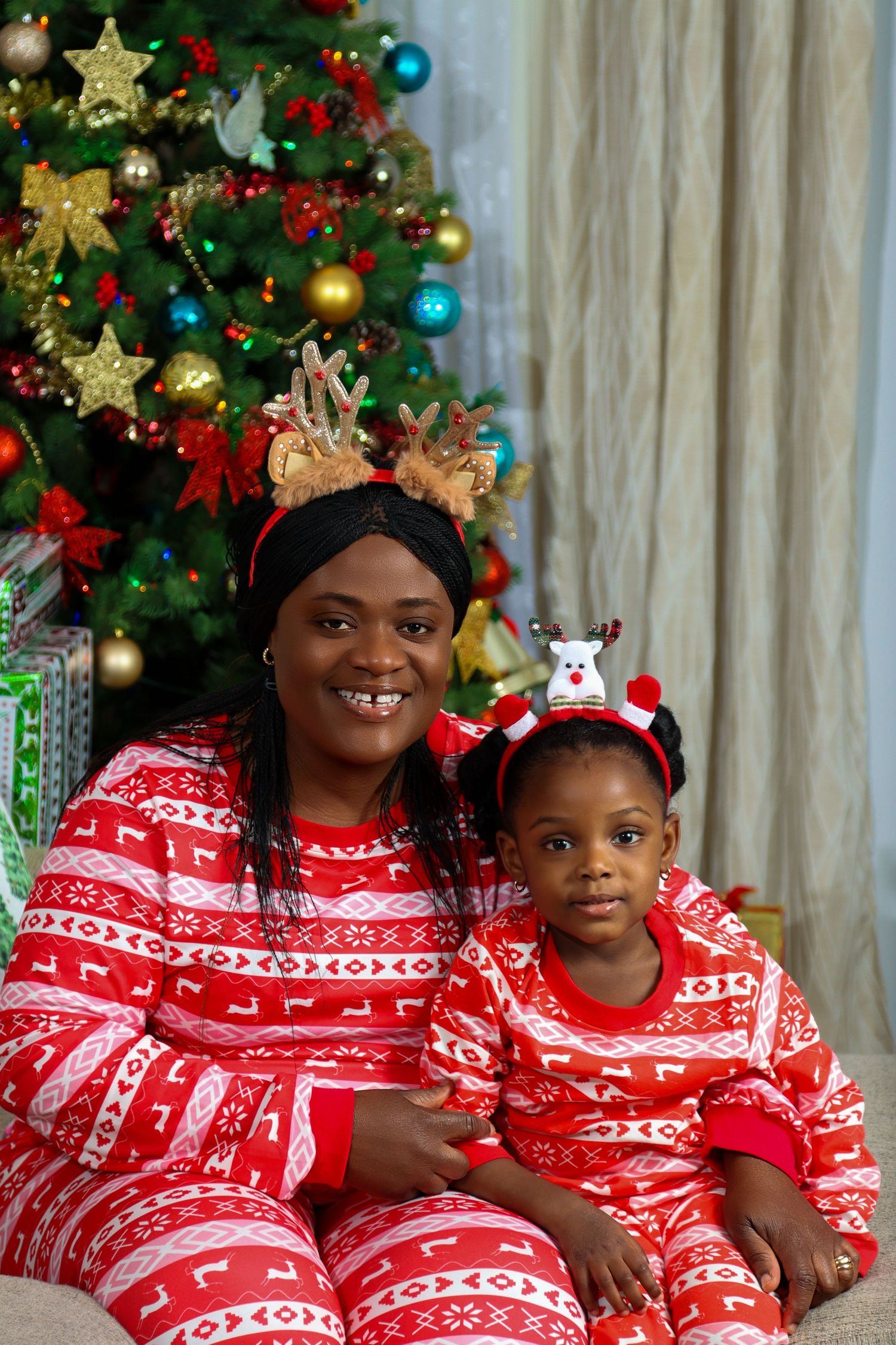 A baby lies sleeping under a decorated Christmas tree with red ornaments and warm glowing lights.