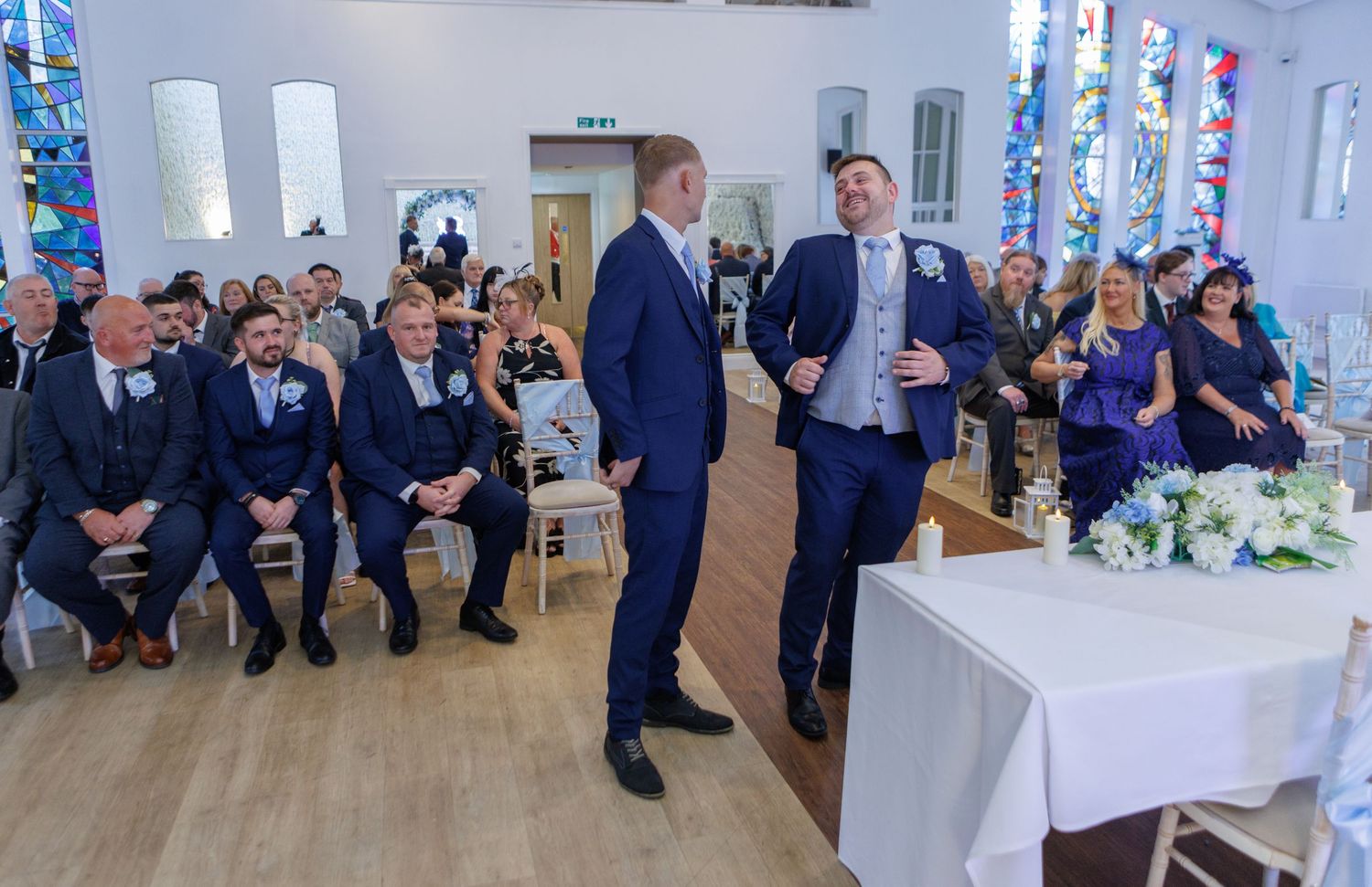 A panoramic view of a wedding reception venue with guests seated along the walls in a bright white room.
