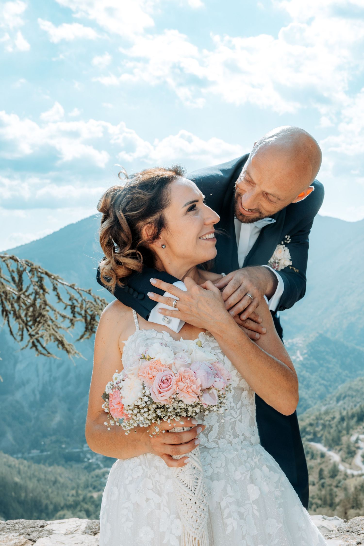Wedding couple embraces against mountain backdrop with dramatic cloudy sky.