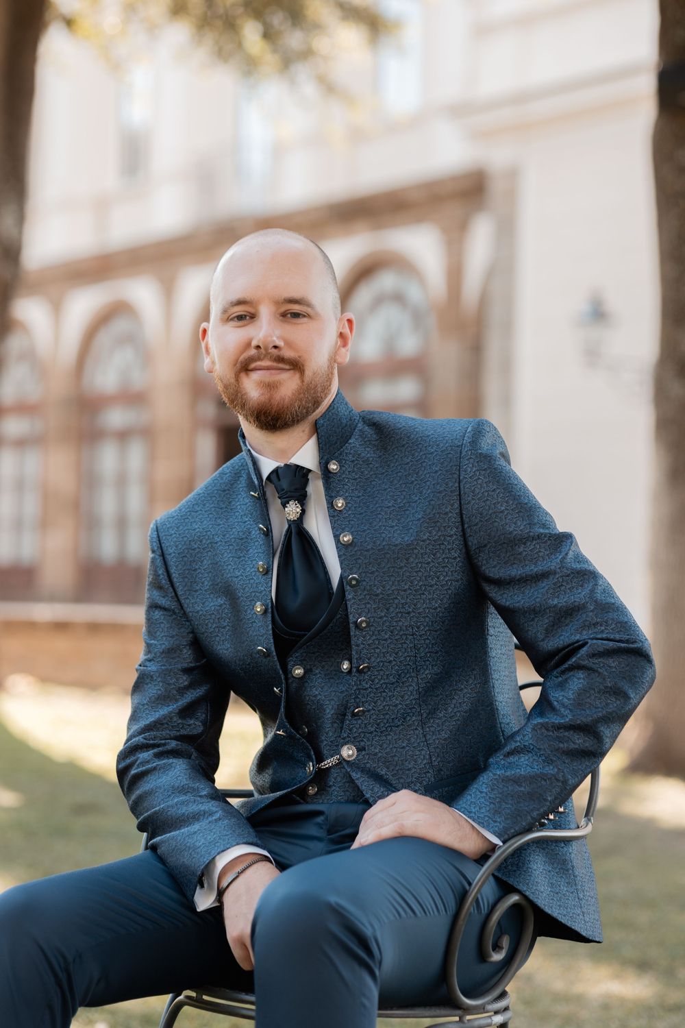 Groom in a dark blue three-piece suit poses outdoors in a series of portraits.