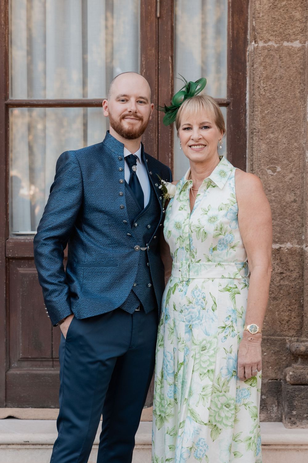 Wedding guests in formal attire pose together outside a historic building entrance.