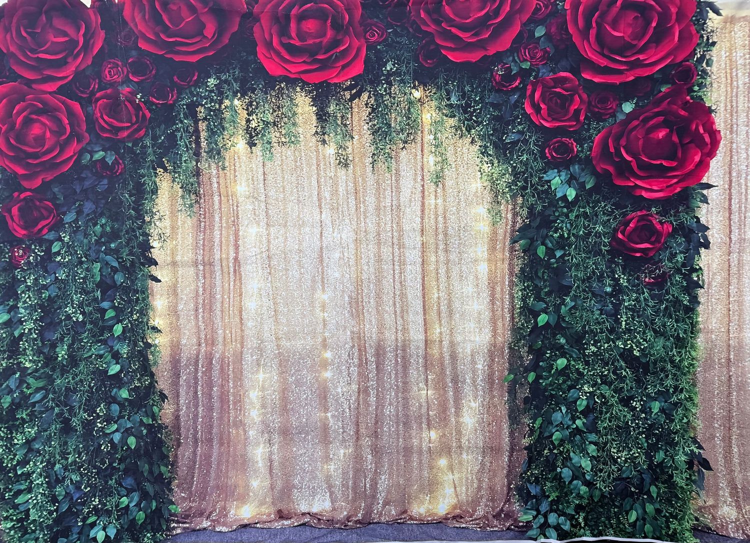 Pink roses adorn the top of a rustic backdrop with greenery and sheer curtains for an elegant wedding photo setting.
