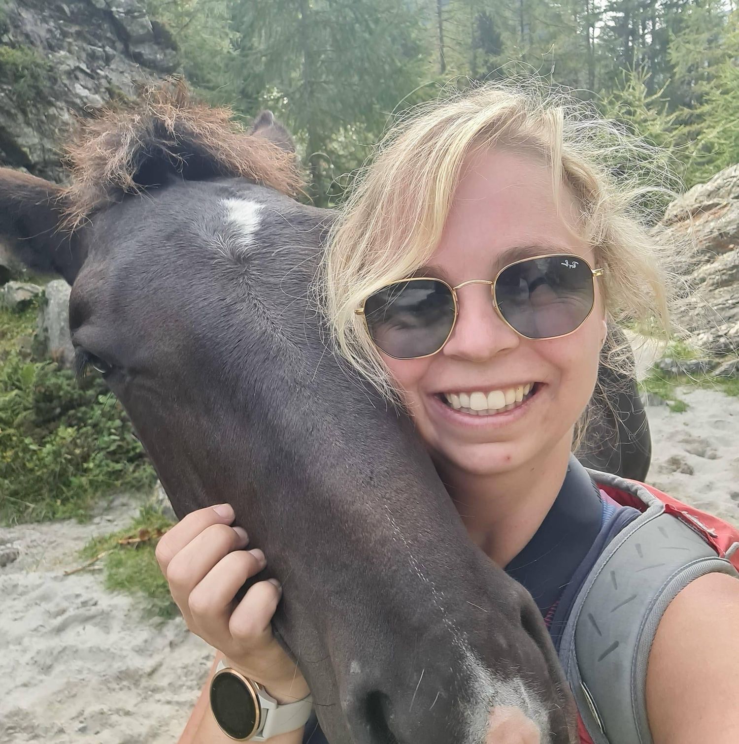 A close-up selfie with a friendly black horse against a forest backdrop while wearing sunglasses.