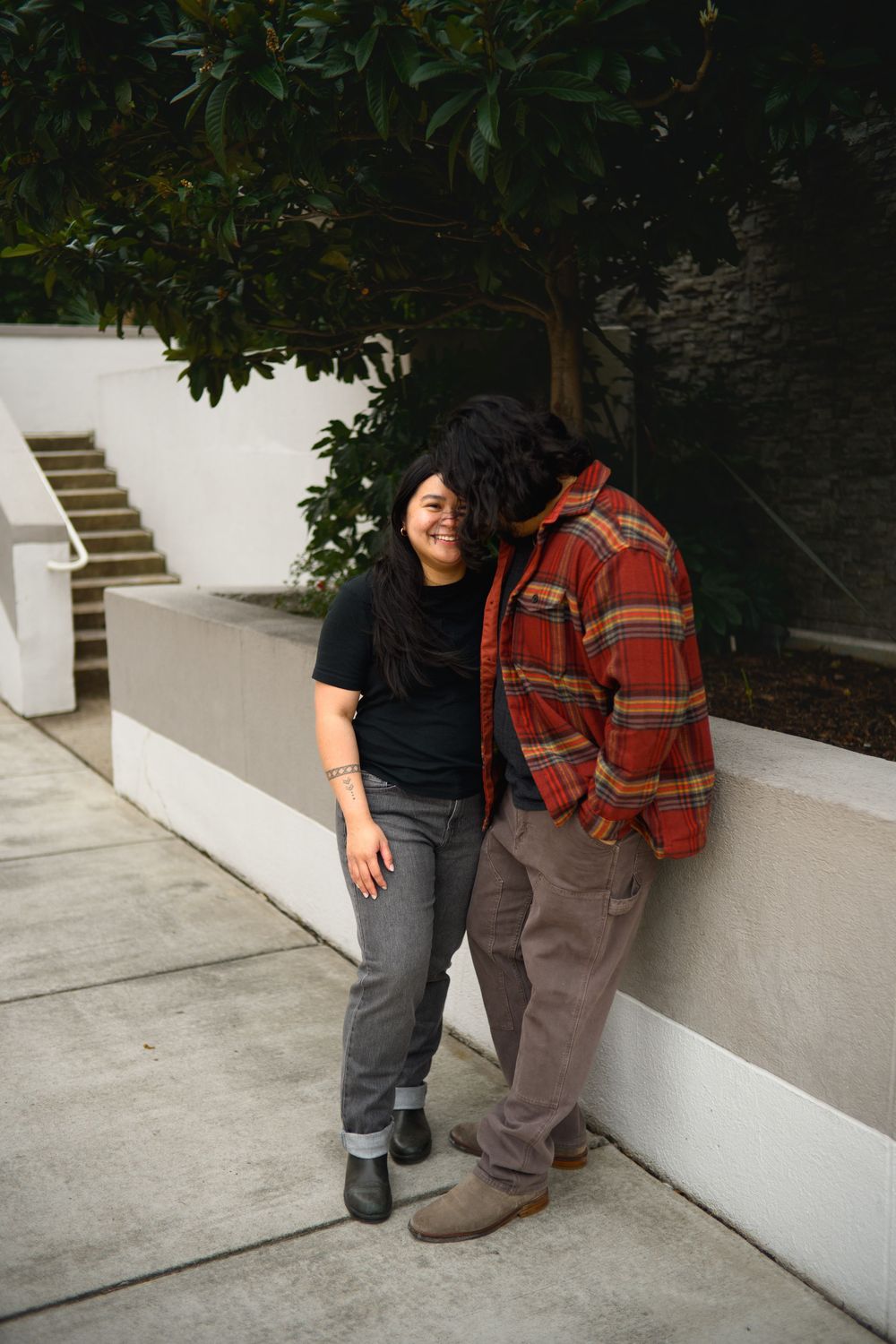 A person in a black shirt and jeans sits on white concrete steps with a red plaid backpack.