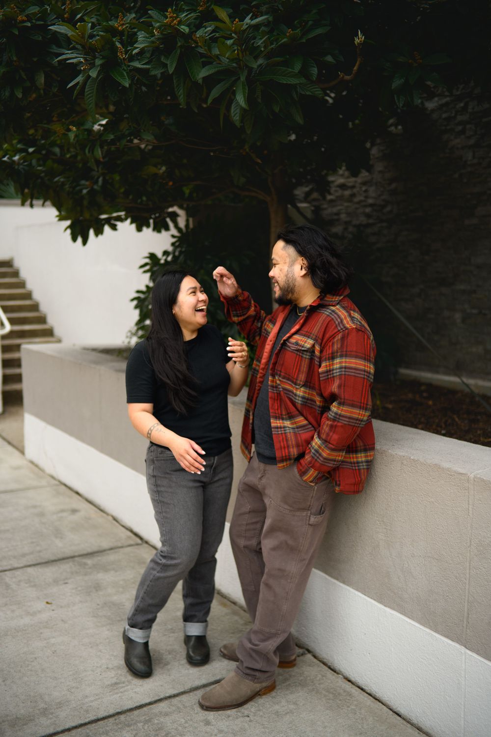 A couple shares a sweet moment against a white wall wearing casual attire and plaid in this romantic photo series.