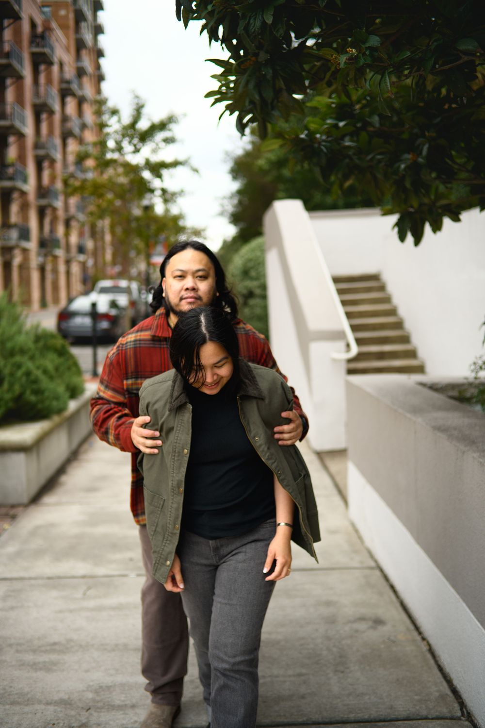 A couple walking together on a sidewalk near a modern apartment building on an overcast day.