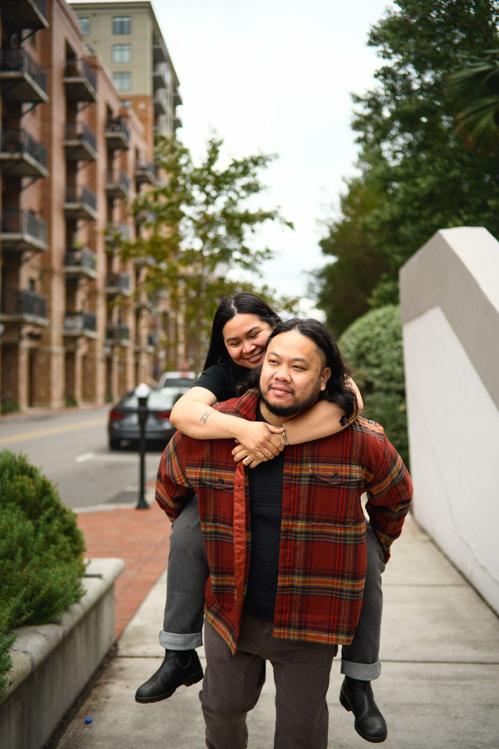 A playful piggyback ride sequence captured on an urban sidewalk with brick buildings in the background.