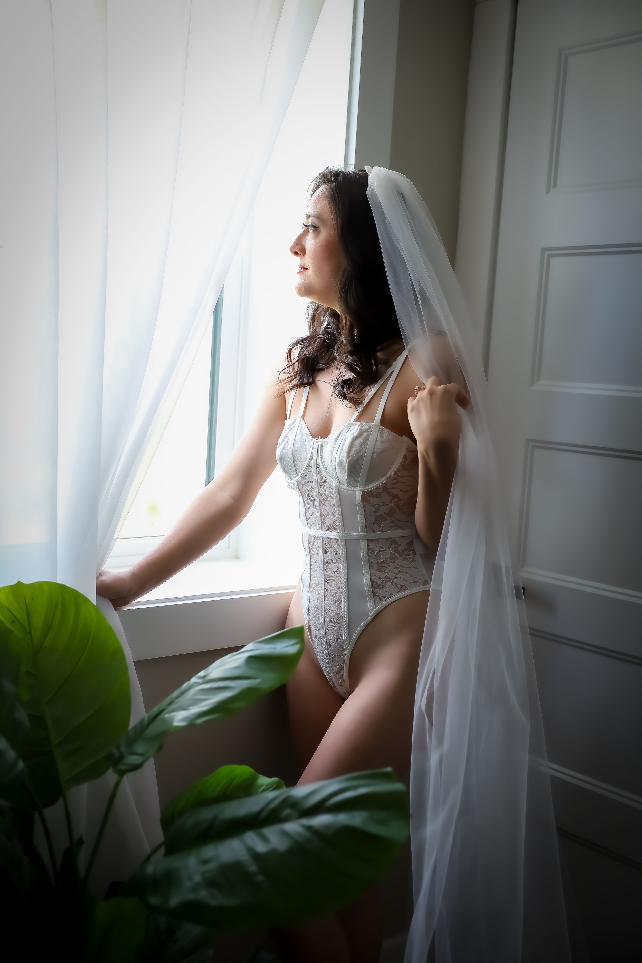 Ethereal bridal boudoir portrait by window with white veil and bodysuit.
