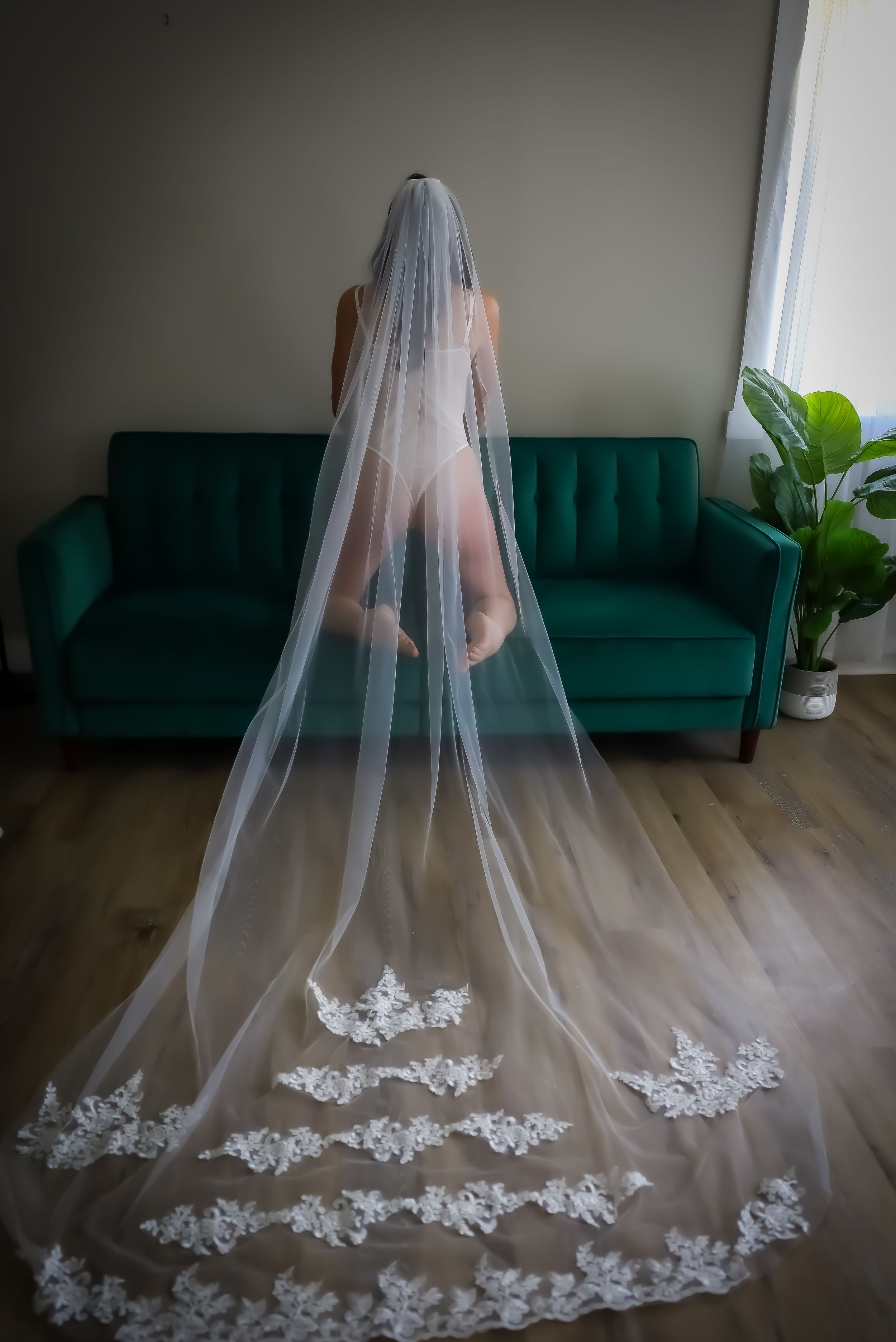 Dramatic bridal portrait with long lace-trimmed veil against emerald green couch.