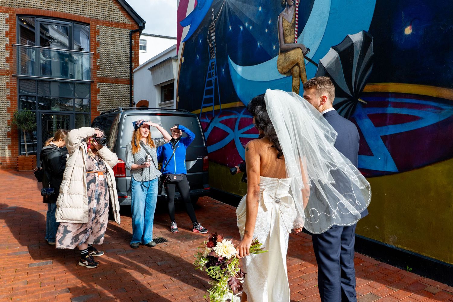 Wedding party poses in front of vibrant street art mural featuring blue and colorful geometric designs.