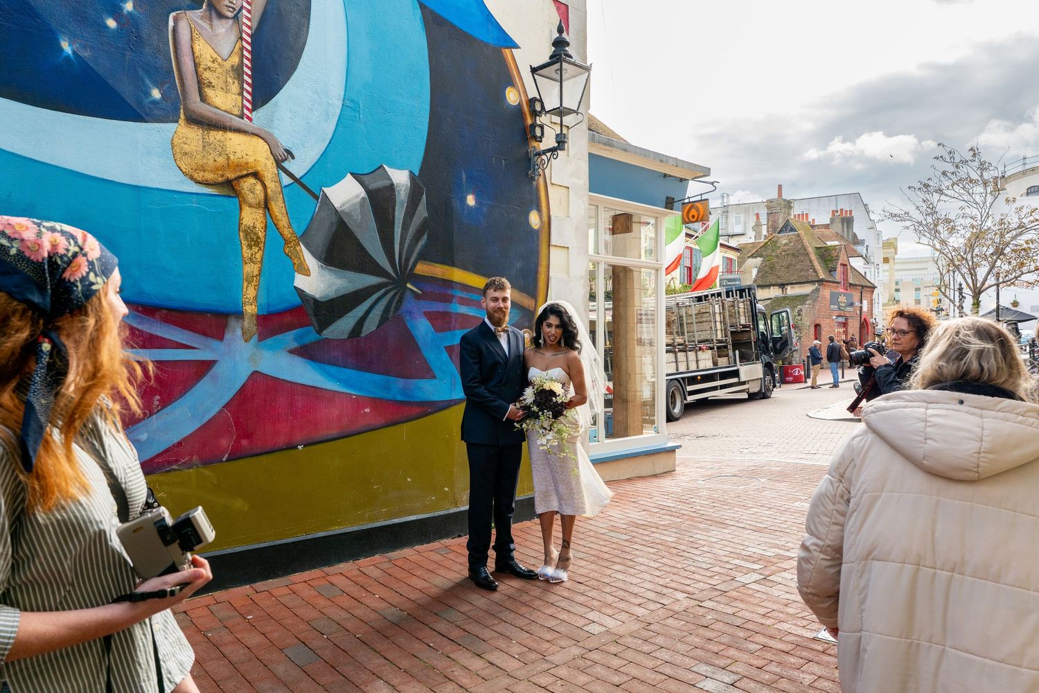 Outdoor wedding photoshoot with bridal party against colorful urban wall art backdrop.