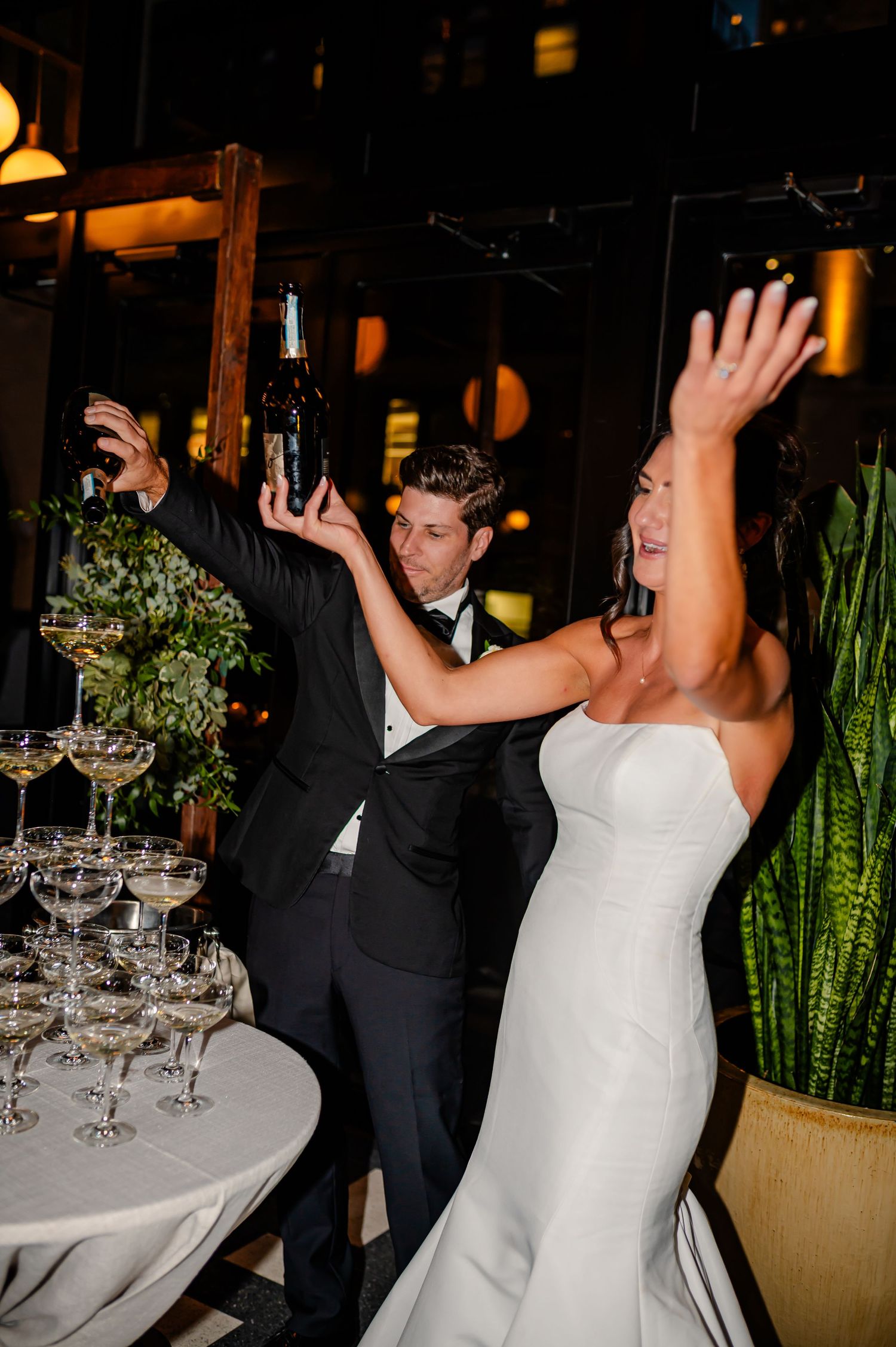 A bride and groom dance together during their wedding reception with wine glasses on tables in the background.
