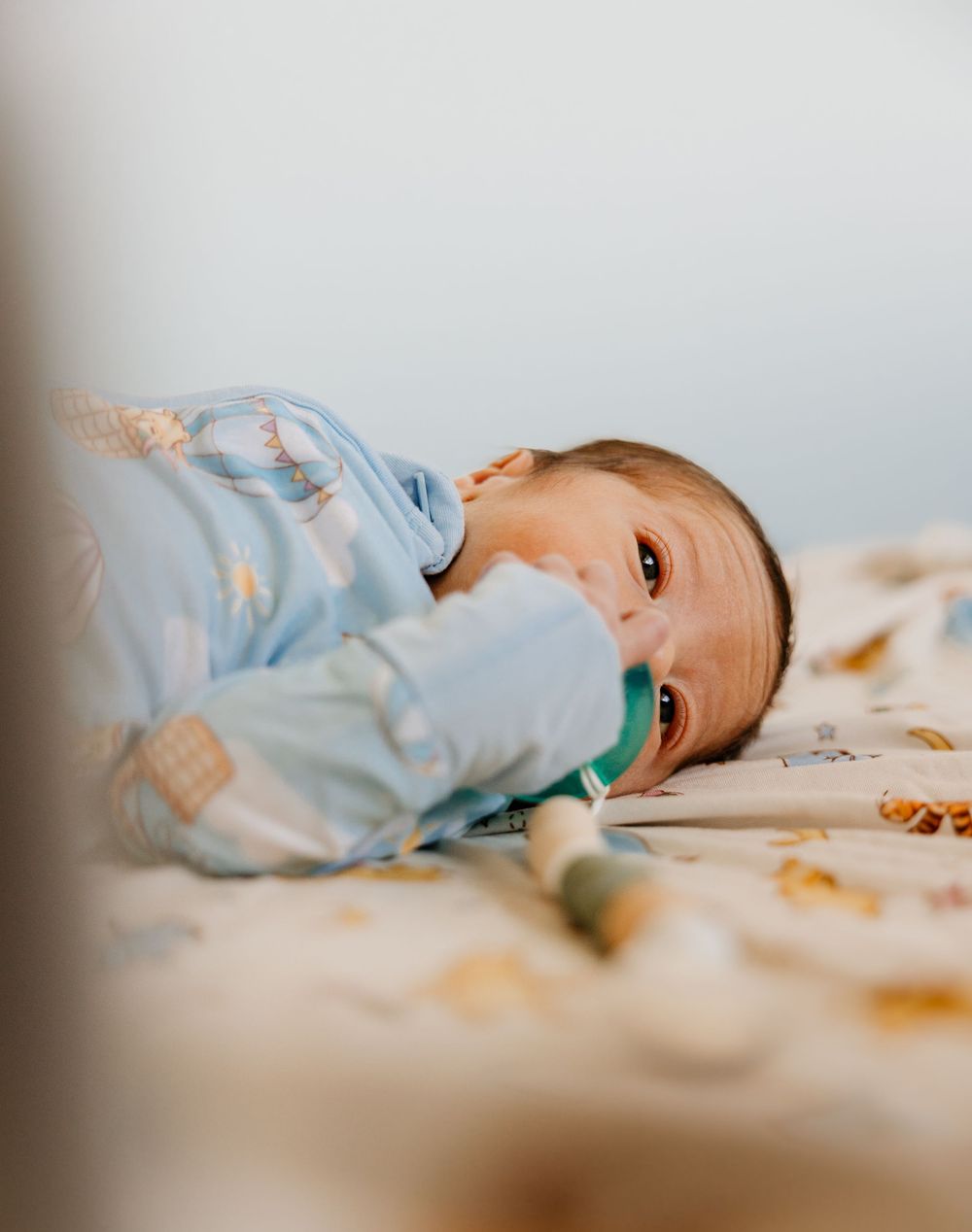 A baby in light blue clothing rests on a soft cream-colored surface in a series of gentle poses.