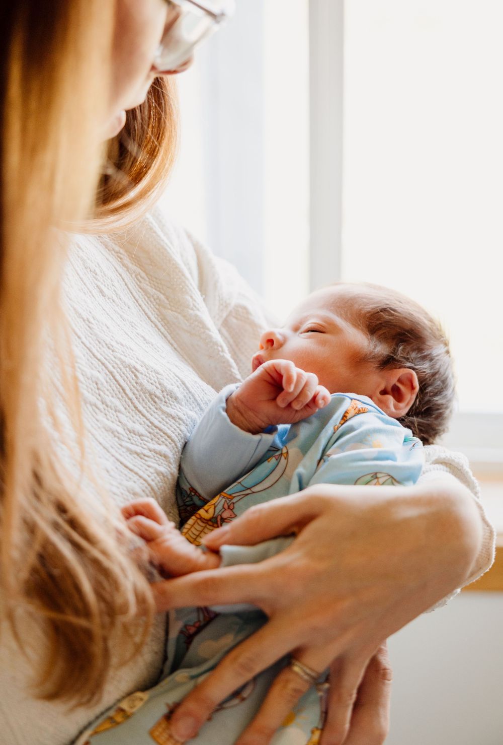 A tender moment between parent and newborn baby in soft natural light by a window.