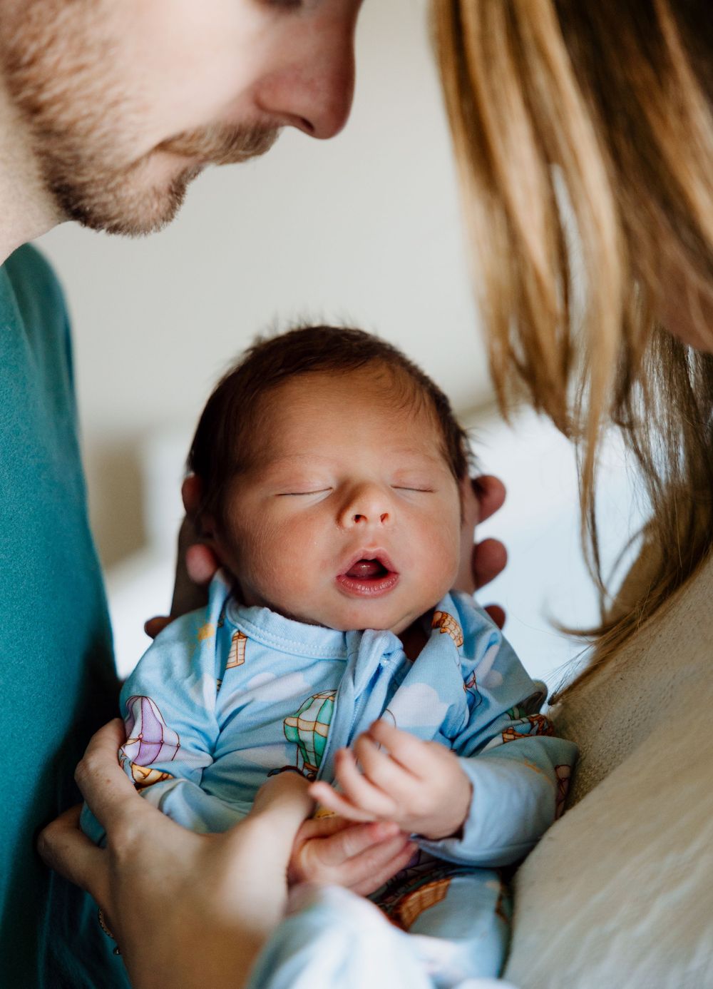 A series of four tender moments showing a baby in light blue clothing yawning and being cradled.