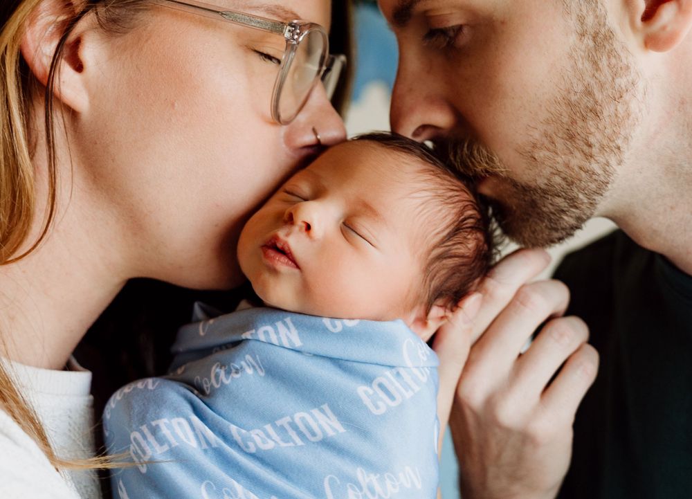 A loving couple shares tender kisses with their baby in a series of intimate black and white photographs.