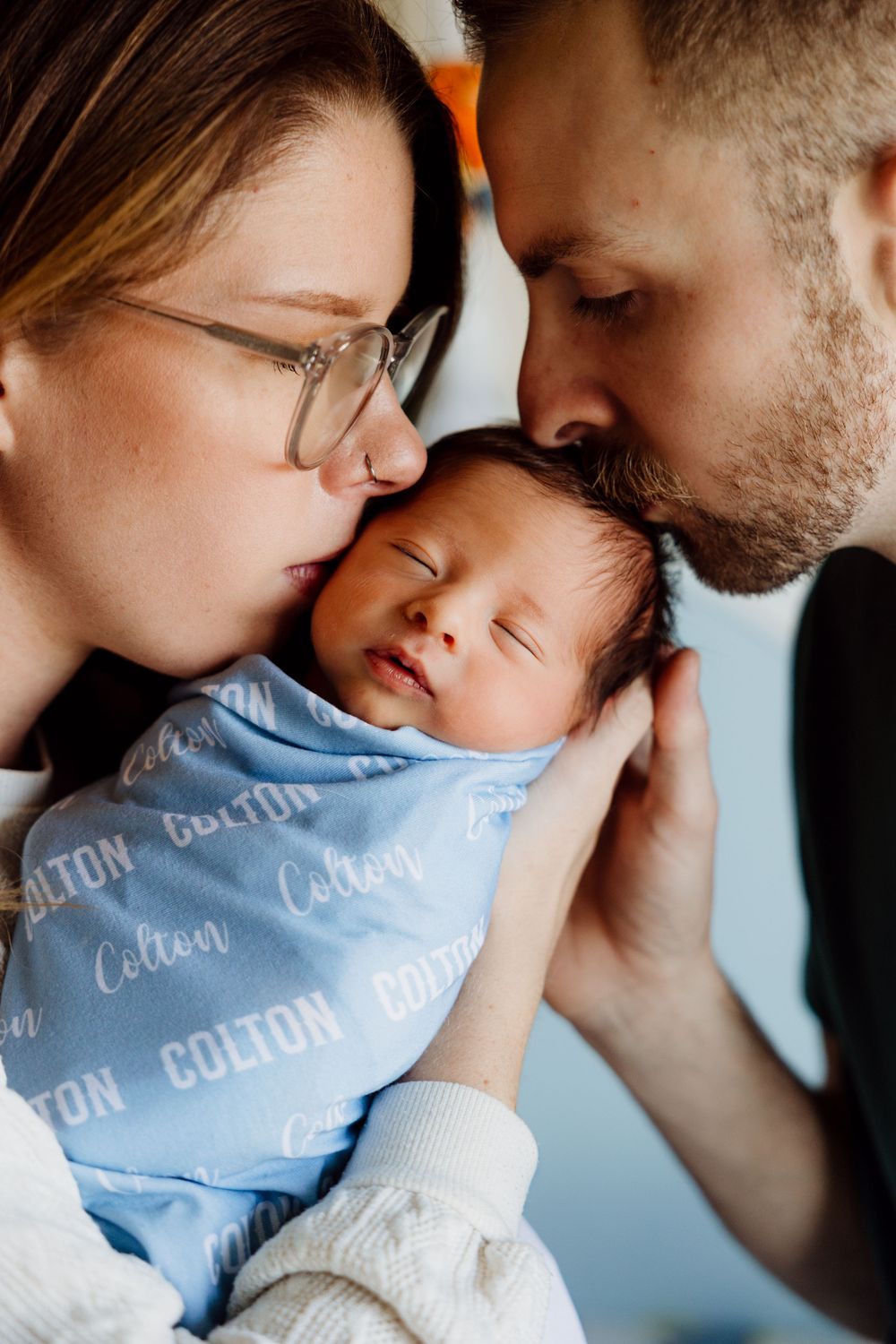 Intimate close-up shots of parents bonding with their newborn baby in blue clothing.