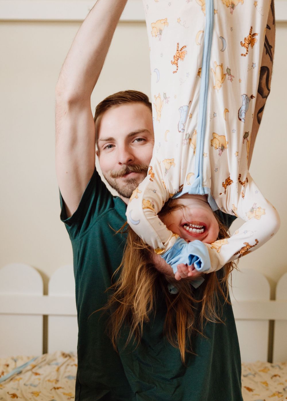 Playful moment captured as two people share laughter and joy while playing on a bed with teddy bear print curtains.