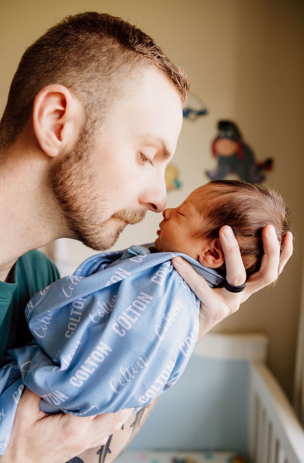 A tender moment between a father and newborn baby in a light blue onesie as they share a gentle nose kiss.