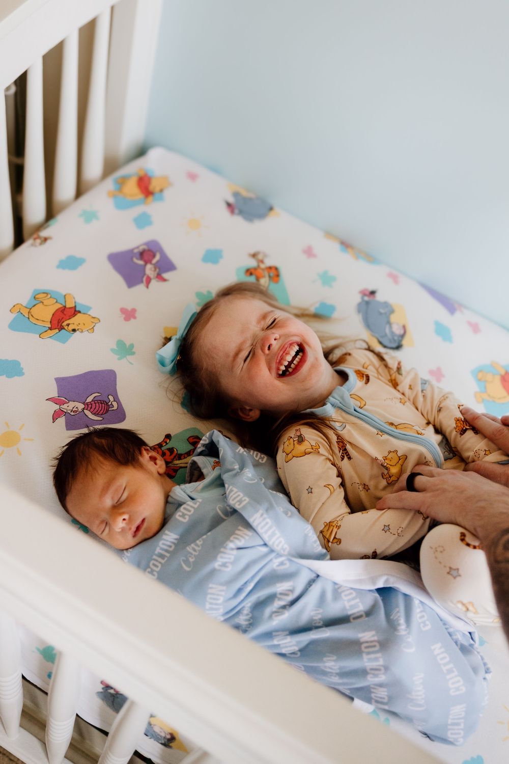 A series of photos showing a laughing child in a crib with colorful bedding and white rails.