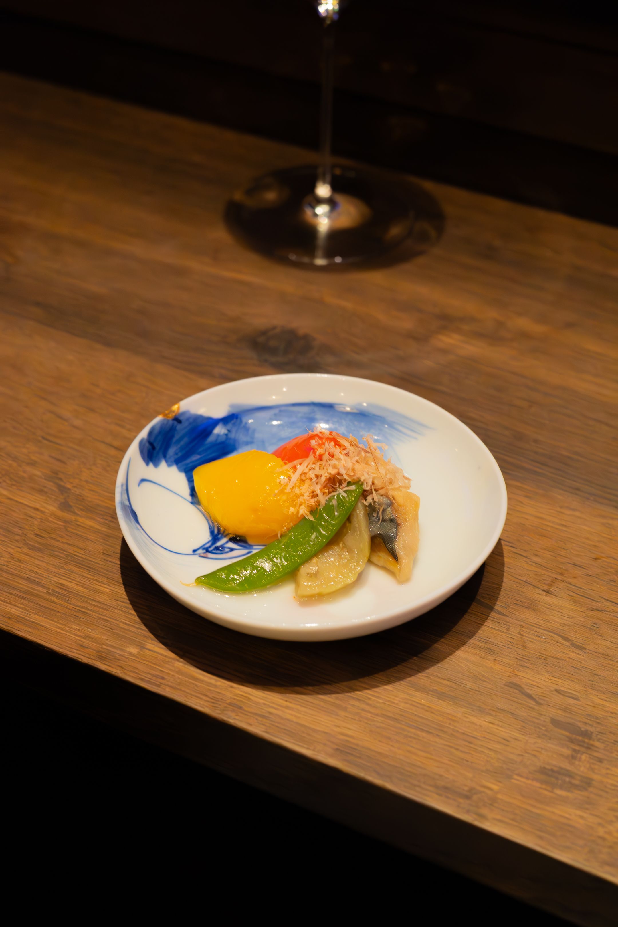 A series of minimalist plated dishes on a wooden counter showing different courses in dim lighting.