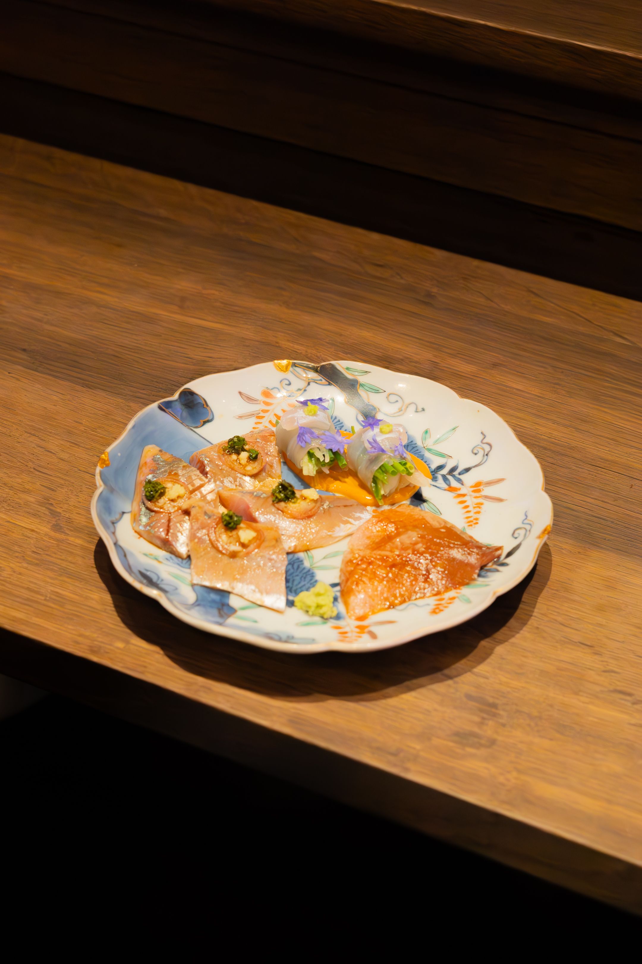 Elegantly arranged sashimi platter with colorful fish, garnishes and blue accents on a decorative white plate.