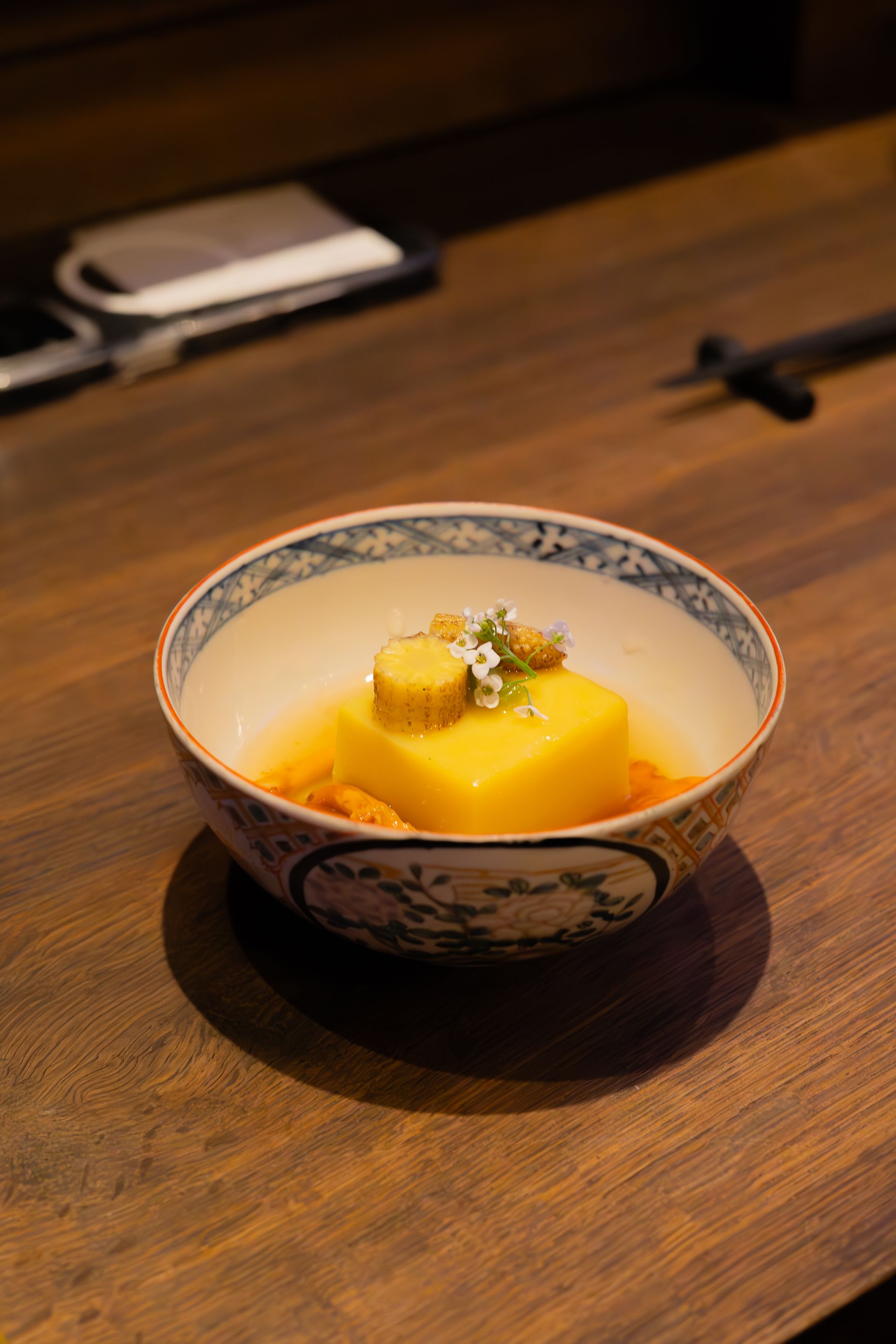 Yellow dessert dish served on a traditional patterned plate against a dark wooden table surface.